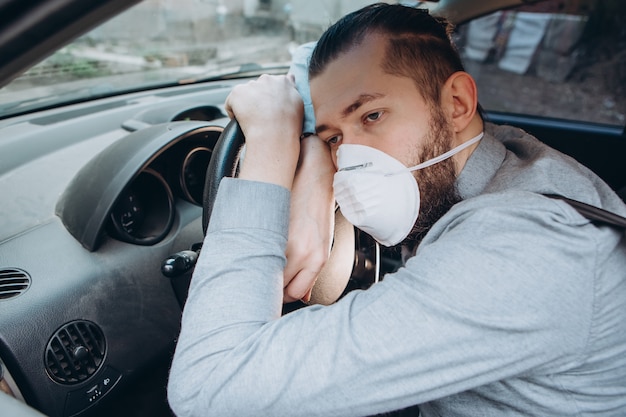 Hombre en camisa y máscara médica se sienta al volante del coche.