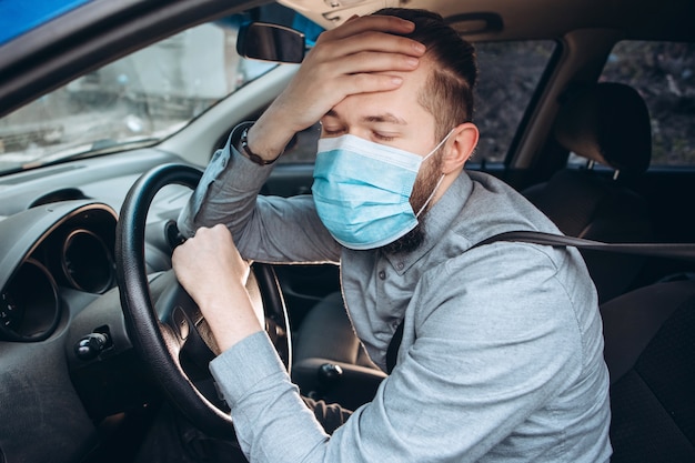 Hombre en camisa y máscara médica se sienta al volante del coche.