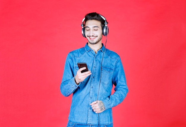 Hombre en camisa de mezclilla con auriculares, tomando su selfie o haciendo una videollamada.