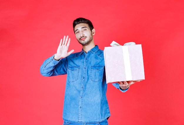 Hombre en camisa de mezclilla sosteniendo una caja de regalo púrpura atada con cinta blanca.