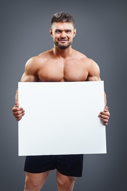 Foto hombre sin camisa muscular feliz que muestra y que muestra el cartel