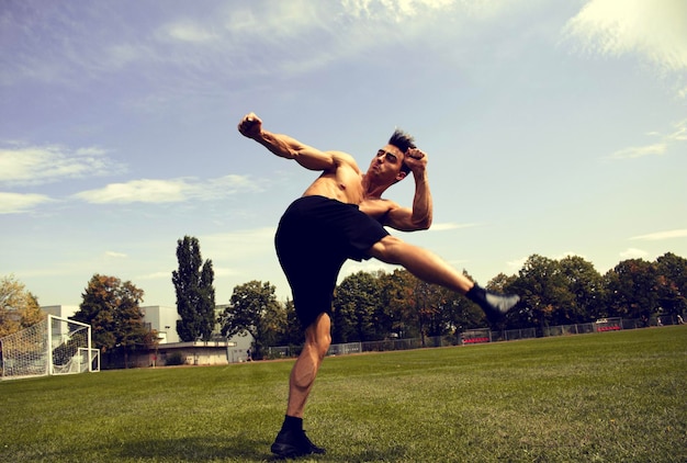 Hombre sin camisa pateando en el campo contra el cielo