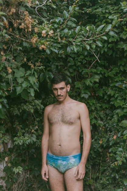 Foto hombre sin camisa de pie contra las plantas