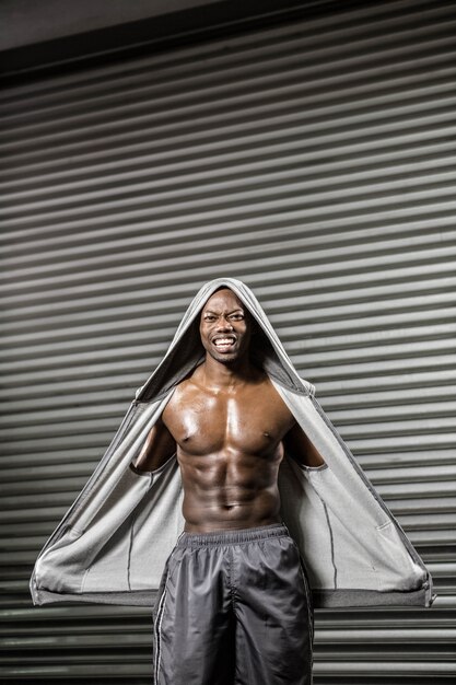 Hombre sin camisa de pie con jersey gris en el gimnasio de crossfit