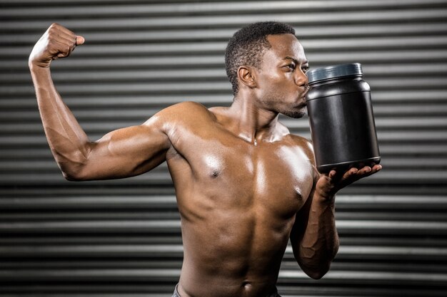 Hombre sin camisa que muestra bíceps y besos puede en el gimnasio de crossfit