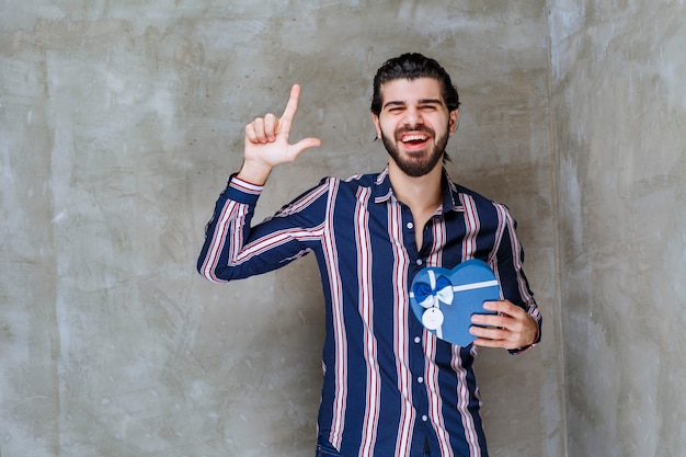 Hombre de camisa a rayas sosteniendo una caja de regalo con forma de corazón azul