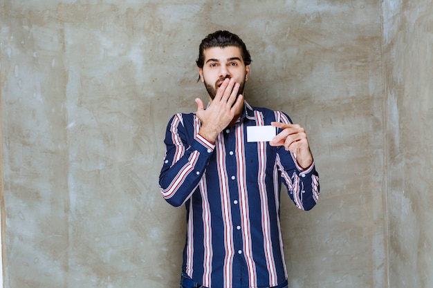 Hombre de camisa a rayas sosteniendo su tarjeta de visita y se siente sorprendido