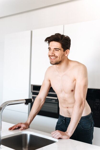 Hombre sin camisa sonriente de pie en la cocina