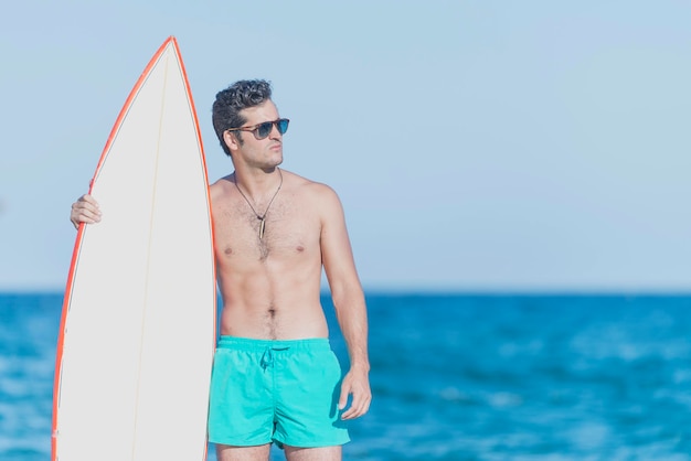 Hombre sin camisa sosteniendo una tabla de surf mientras está de pie contra el mar