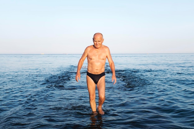 Hombre sin camisa vadeando en el mar contra el cielo