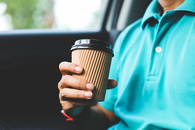 Un hombre con la camisa verde que sostiene una taza de café en el coche.