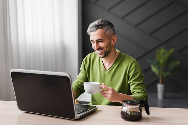 Hombre de camisa verde sonríe y usa su computadora portátil