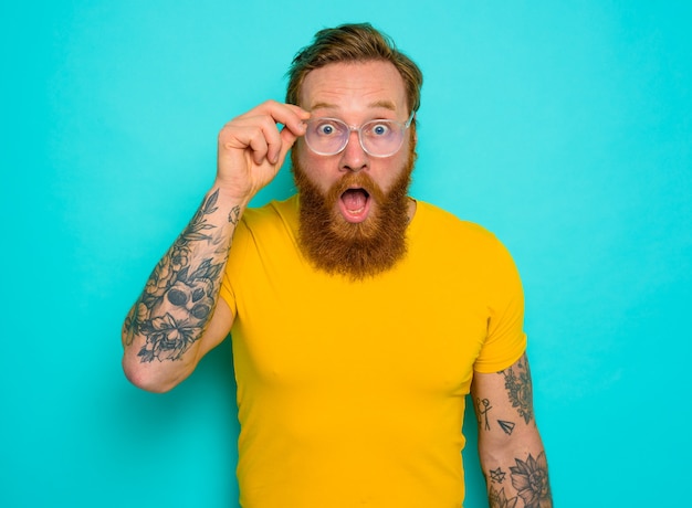 Hombre con camiseta amarilla y barba está sorprendido por algo