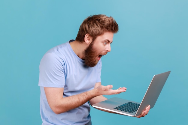 Hombre en camiseta azul apuntando con el dedo a la pantalla de la computadora portátil sorprendido con su victoria no puede creer