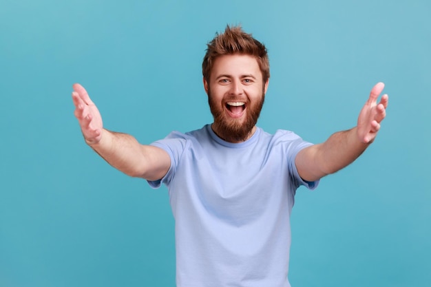 Hombre en camiseta azul estirando las manos a la cámara y sonriendo ampliamente va a abrazar