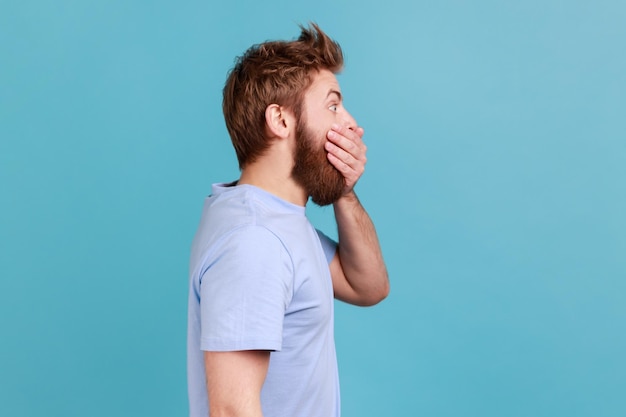 Hombre en camiseta azul que cierra la boca manteniendo información secreta mirando el espacio lateral