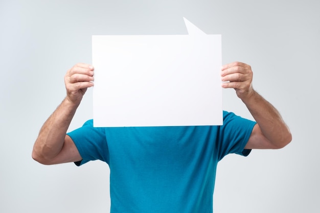 Hombre en camiseta azul sosteniendo copyspace en blanco cerca de su rostro Hombre sin rostro con cartel blanco