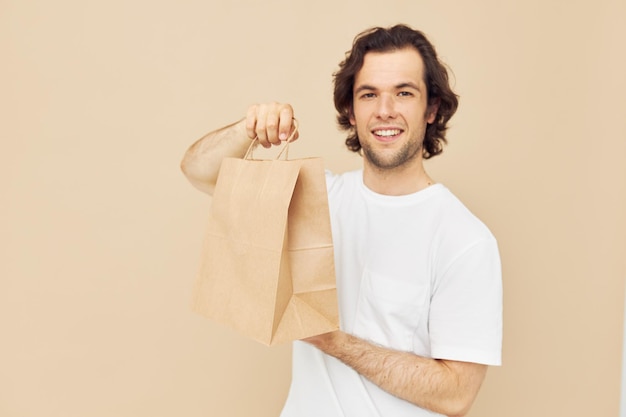 Hombre en una camiseta blanca con bolsa de papel de fondo beige