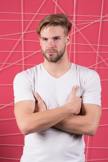 Hombre con camiseta blanca con las manos cruzadas Chico con rostro barbudo sin afeitar Macho con cabello rubio corte de pelo elegante Cuidado del cabello en salón o barbería Belleza y aseo masculino