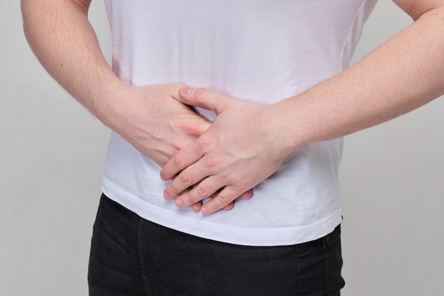 Un hombre con una camiseta blanca se masajea el estómago debido al dolor intenso en el páncreas, el intestino.