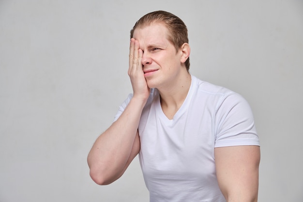 Un hombre con una camiseta blanca se masajea los ojos, un dolor terrible debido a la inflamación.