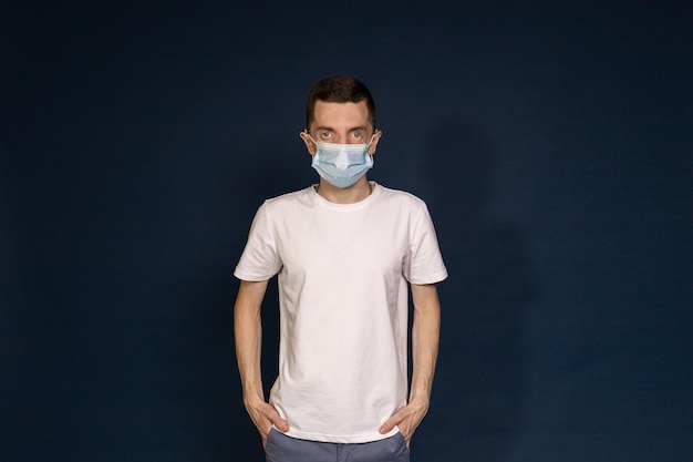 Un hombre con una camiseta blanca y una máscara protectora se alza contra un fondo azul.