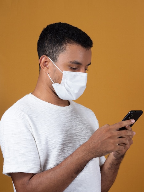 Foto hombre de camiseta blanca con máscara con teléfono celular en sus manos