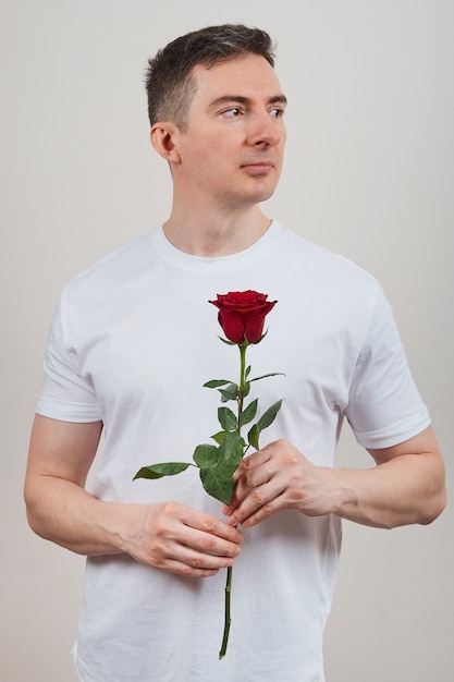 Hombre con una camiseta blanca con una rosa roja en sus manos