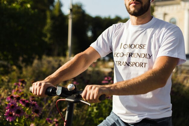 Un hombre con una camiseta blanca sostiene los brazos de su scooter eléctrico mientras viajaba en la superficie borrosa del parque