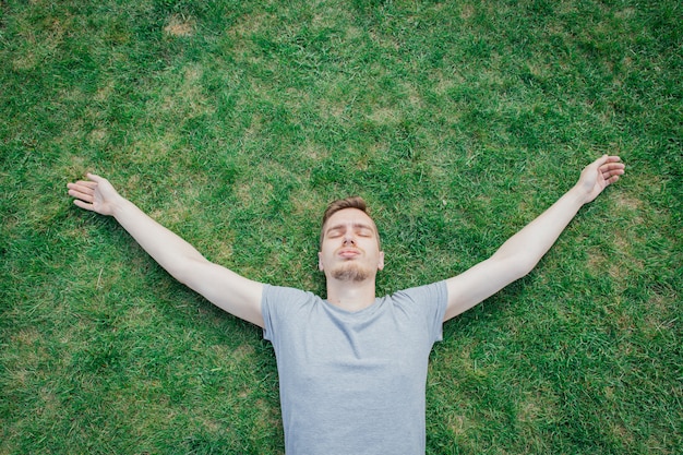 Un hombre en camiseta gris tumbado en la hierba verde, verano. Hombre descansando