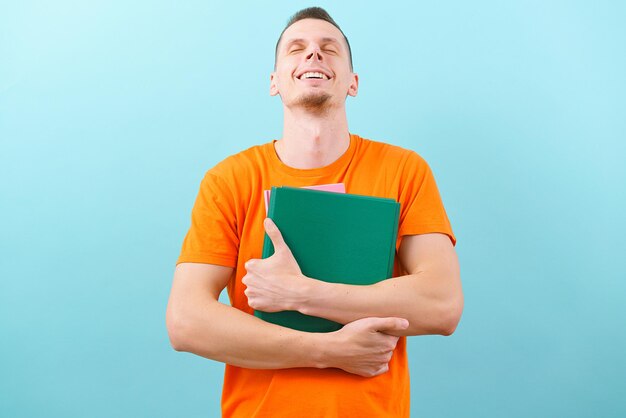 Un hombre con una camiseta naranja sostiene la cabeza erguida y sonríe mientras sostiene archivos aislados en un fondo blanco Smart Looking Office Business Happy Paper Portrait Young Adult Casual Cheer