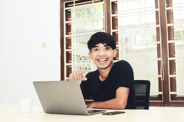 El hombre de la camiseta negra asiática se sentó frente a la computadora portátil con una expresión muy feliz.