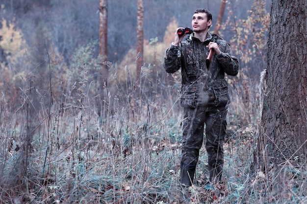 Hombre de camuflaje y con un rifle de caza en un bosque en una caza de primavera