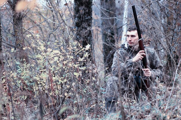 Hombre de camuflaje y con un rifle de caza en un bosque en una caza de primavera