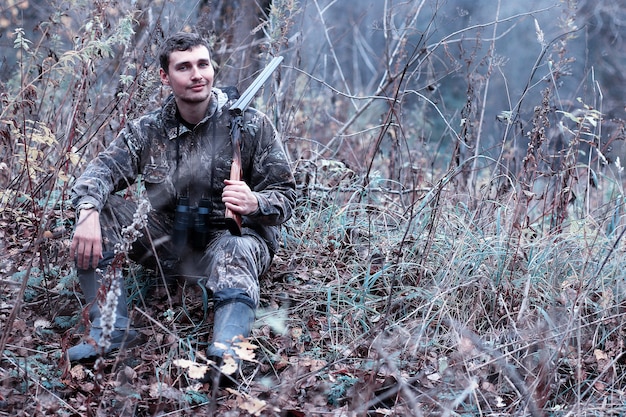 Hombre de camuflaje y con un rifle de caza en un bosque en una caza de primavera