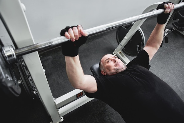 El hombre canoso adulto entrena en equipos de fitness en el gimnasio bombea los músculos de las piernas y los brazos pierde peso Concepto de estilo de vida saludable en la vejez