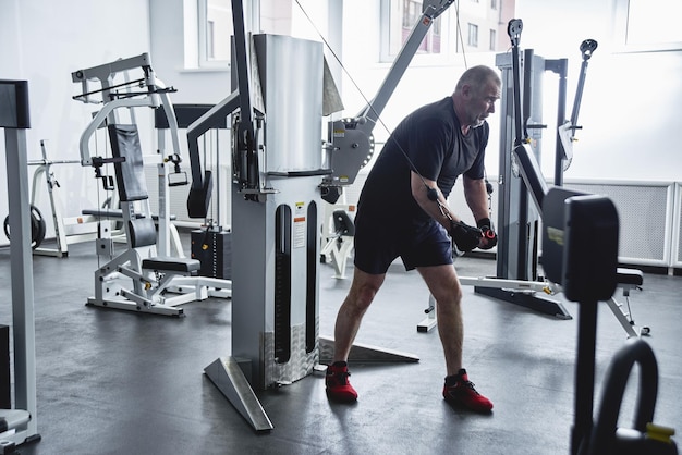 El hombre canoso adulto entrena en equipos de fitness en el gimnasio bombea los músculos de las piernas y los brazos pierde peso Concepto de estilo de vida saludable en la vejez