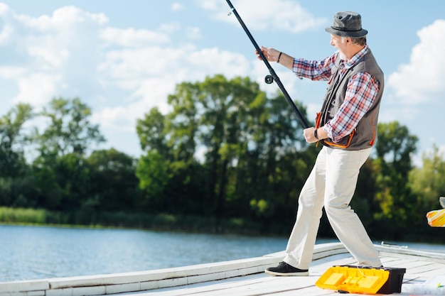 Hombre canoso barbudo tirando de aparejos de pesca mientras pesca