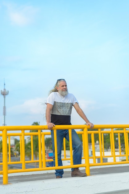 Hombre canoso de pelo largo en un puente peatonal con vistas a la ciudad