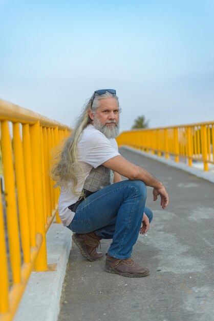 Hombre canoso de pelo largo en un puente peatonal