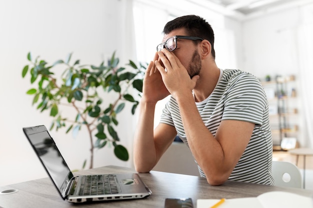 hombre cansado con una computadora portátil trabajando en la oficina de casa