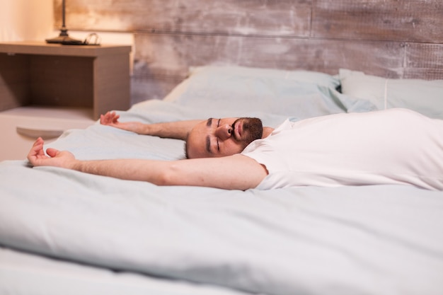 Hombre cansado dormido de espaldas en una cama cómoda.