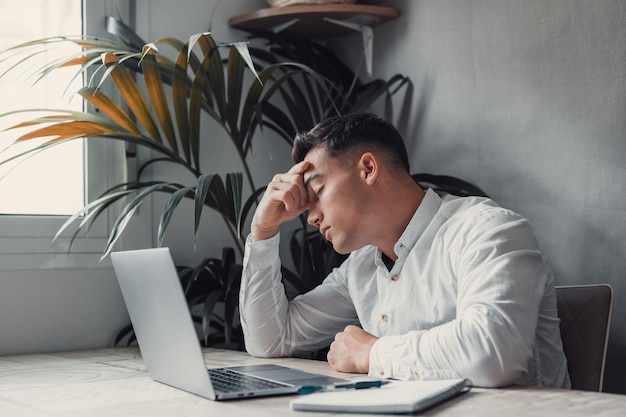 Hombre cansado estresado con dolor que tiene un fuerte ataque de dolor de cabeza terrible después del trabajo con computadora portátil