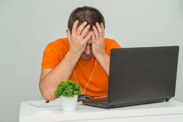 Foto hombre cansado con exceso de trabajo en camisa naranja tiene la cabeza sentada cerca de la computadora portátil. trabajo en línea. concepto de educación en línea