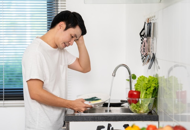 Hombre cansado lavando platos en el fregadero de la cocina en casa