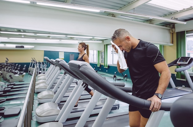 Hombre cansado de secar con una toalla sobre una cinta de correr en el gimnasio