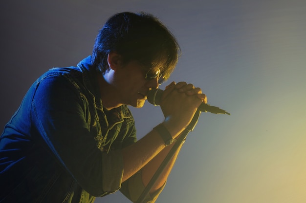 Foto un hombre cantando en un micrófono bajo foco con humo en un escenario