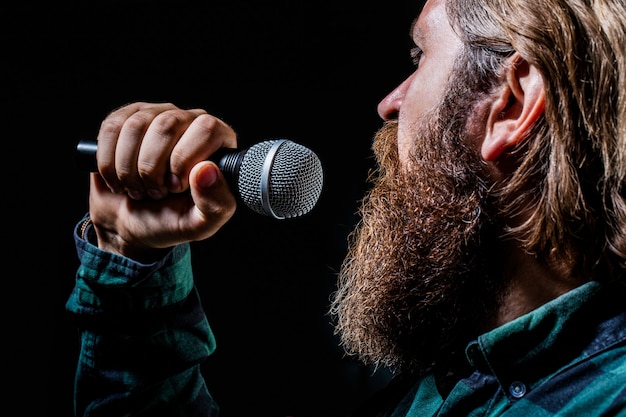 Hombre cantando con micrófonos. Hombre con barba sosteniendo un micrófono y cantando. Hombre barbudo en karaoke canta una canción en un micrófono. Hombre asiste a karaoke.
