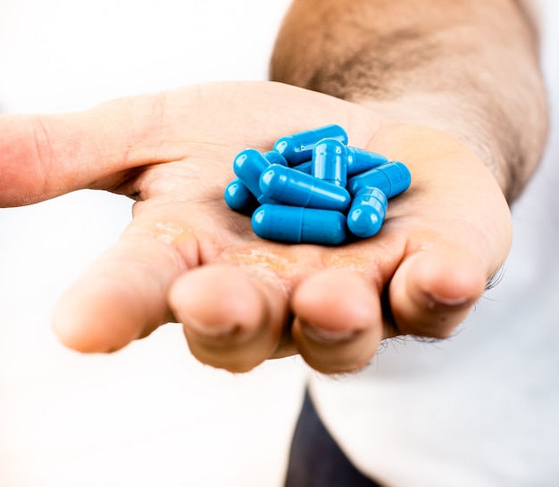 Un hombre con cápsulas de suplemento alimenticio o medicina azul en la mano con fondo blanco.