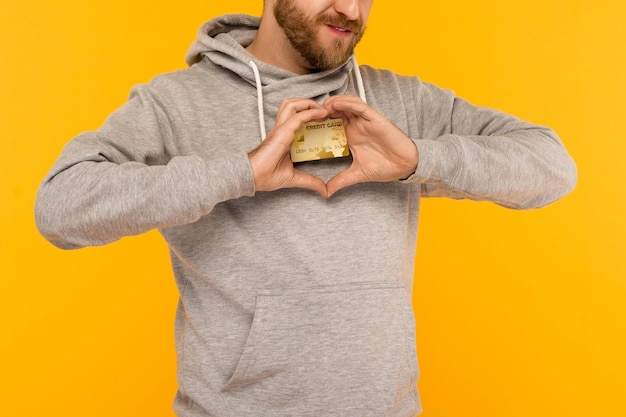 Un hombre con una capucha gris sostiene una tarjeta de crédito en sus manos con un fondo amarillo